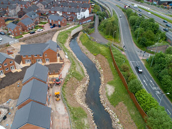 A restored river channel showed flowing with a road on of one side of it and a housing estate on the other