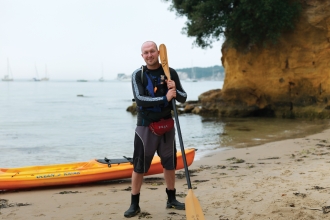 Dan stands on a beach with his kayak