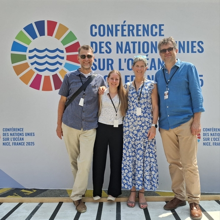 Four Wildlife Trust staff stood in front of the United Nations Oceans Conference sign, smiling at the camera